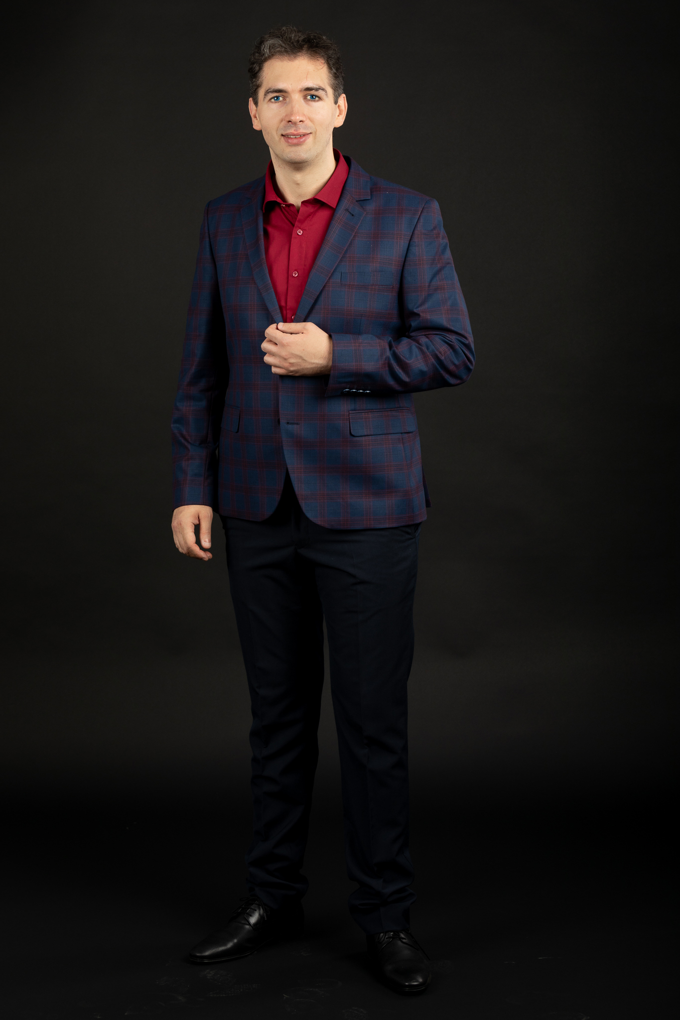 Formal portrait of Christian – tall man with brown hair and blue eyes wearing a suit, against a black background.
